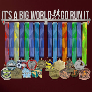 It's A Big World. Go Run It Medal Hanger Display holding colorful ribbons and various sports medals, ideal for runners and athletes.